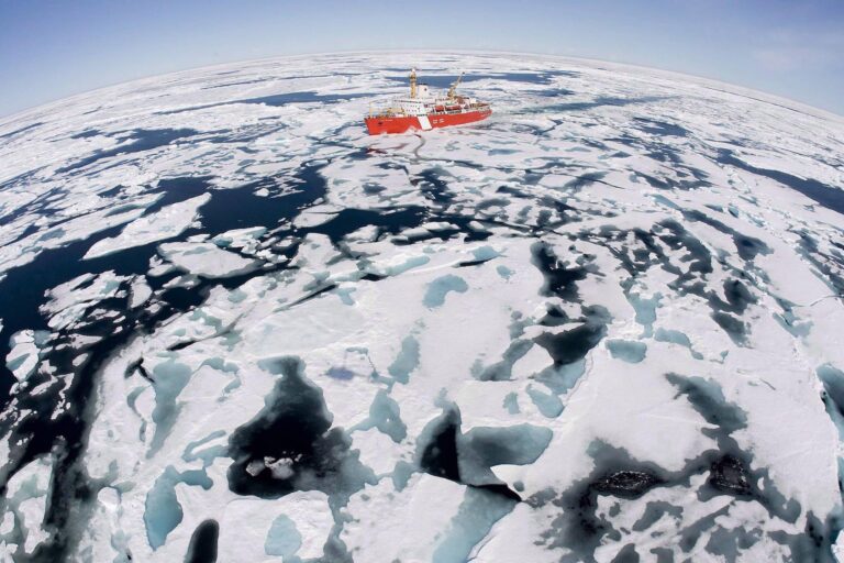 A wide-lens aerial shot of a red Canadian Coast Guard ship amid a sea of white ice pans. The effect of the lens exaggerates the curvature of the horizon.
