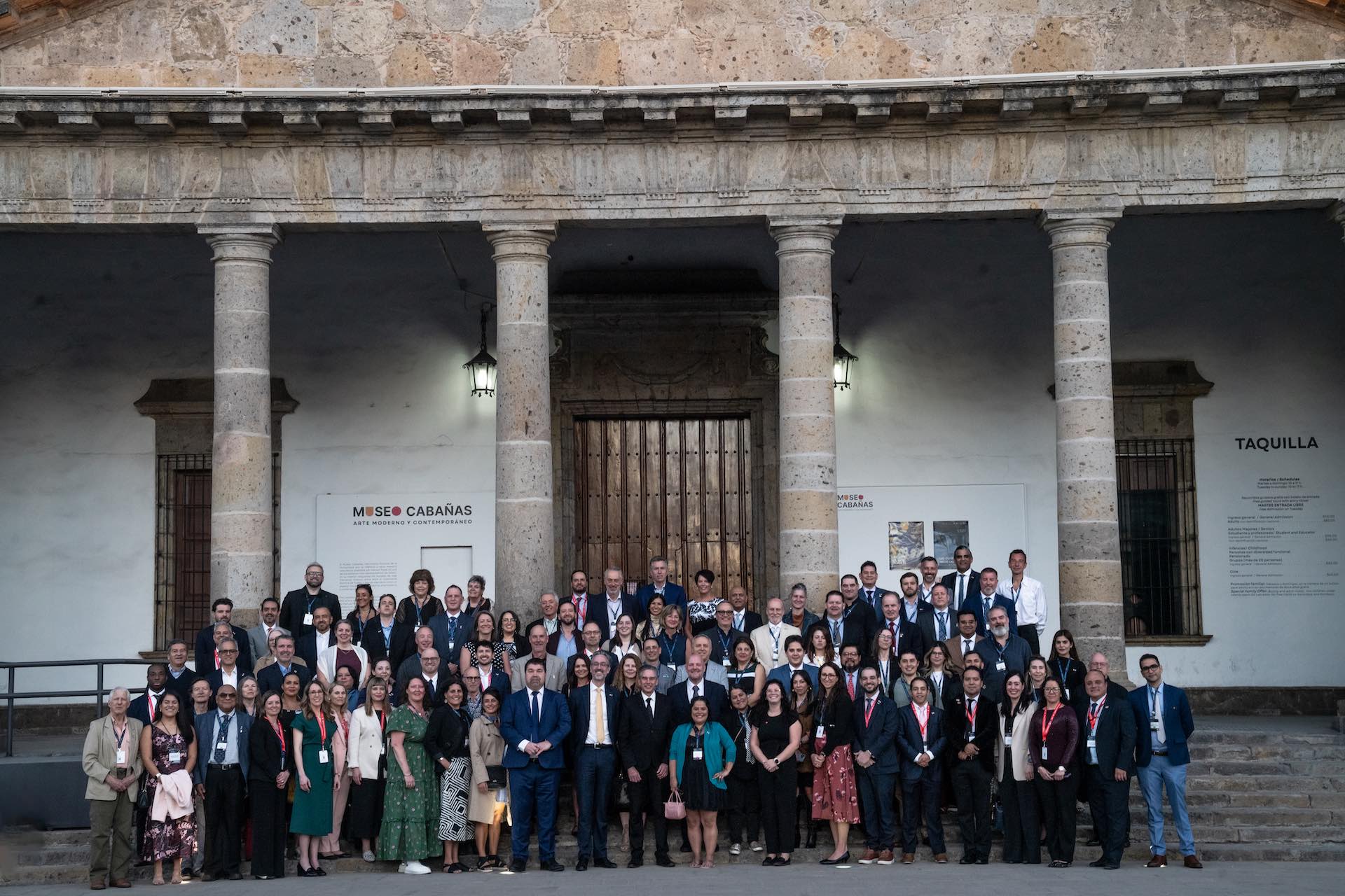 A group shot of about 75 people taken in front of majestic stone building with columns at its entrance.