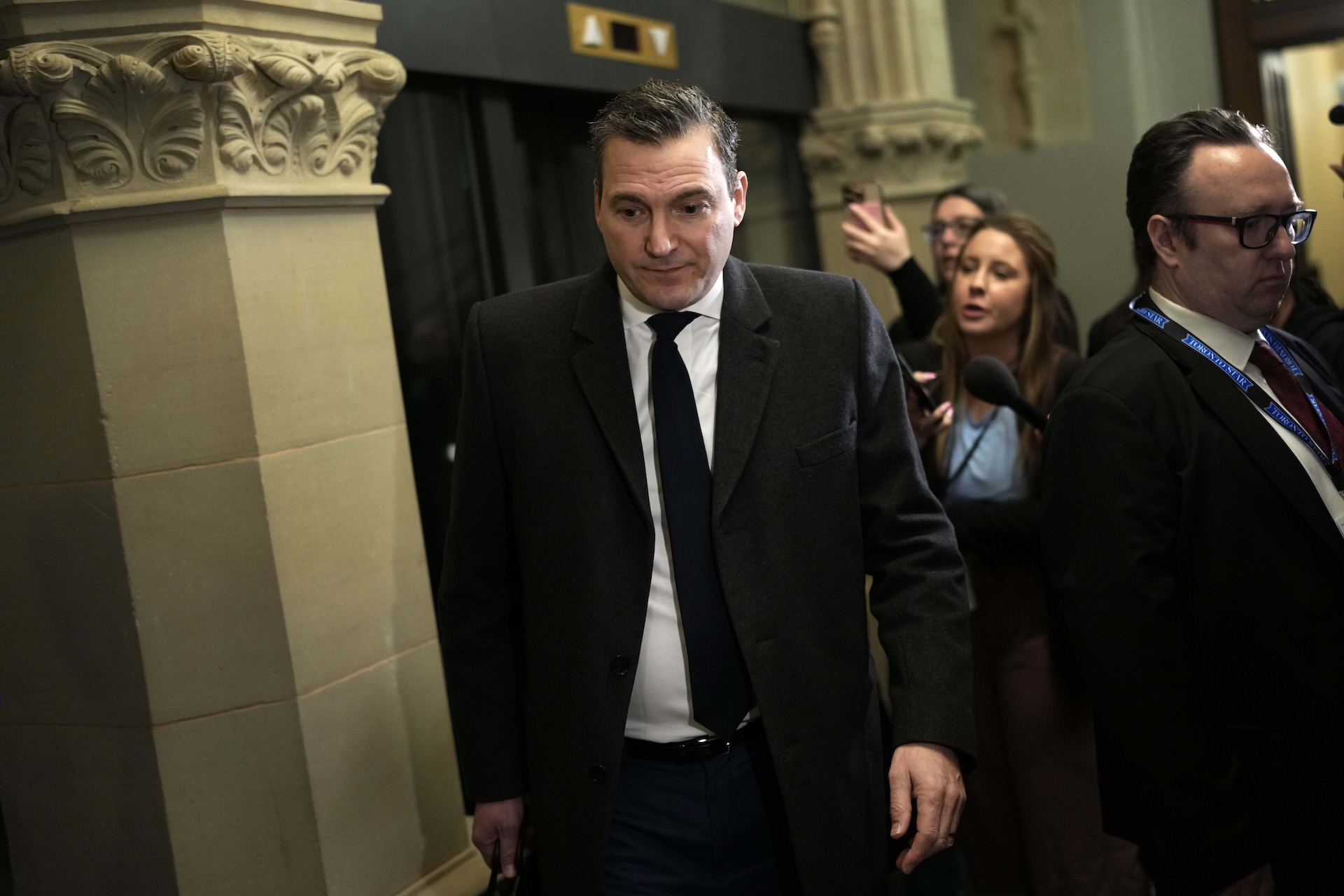A shot of Evan Solomon walking through a parliamentary corridor with a grim expression on his face.