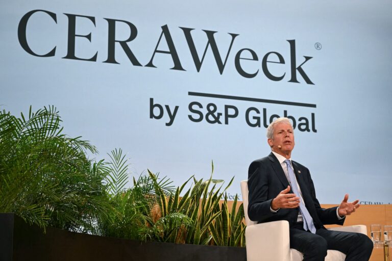 A man wearing a suit and tie sits on a stage. He speaks into an earset microphone and gestures with his hands. A screen behind the speaker reads CERAWeek by S&P Global.