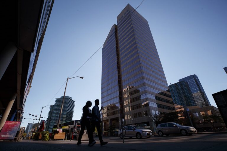 A high-rise building with glass exterior towers over on a street in Toronto. Two pedestrians are visible in the foreground.