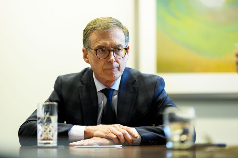 Tiff Macklem sits at a desk, a pair of water glasses visible in the foreground.