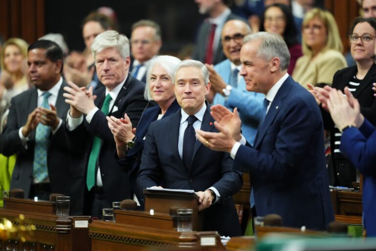 Prime Minister Mark Carney and Finance Minister Francois-Philippe Champagne stand and applaud inside of the House of Commons.