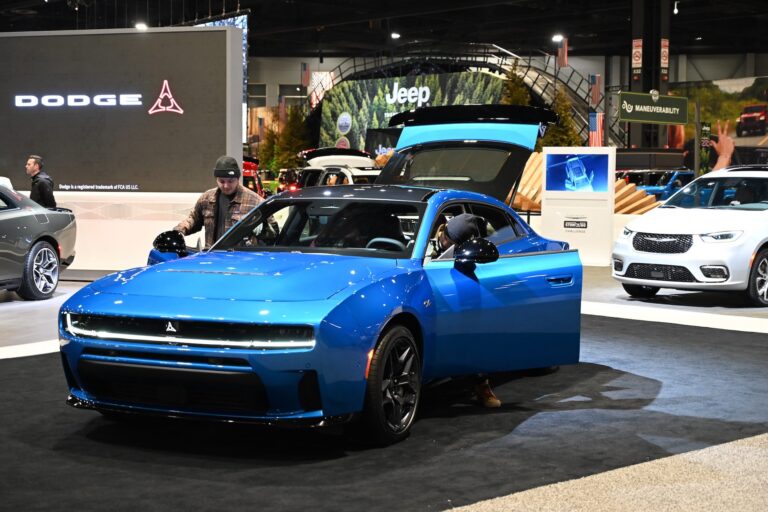 A shot of a blue Dodge Charger on the floor of an auto show, with its doors and trunk open and attendees checking out the interior.
