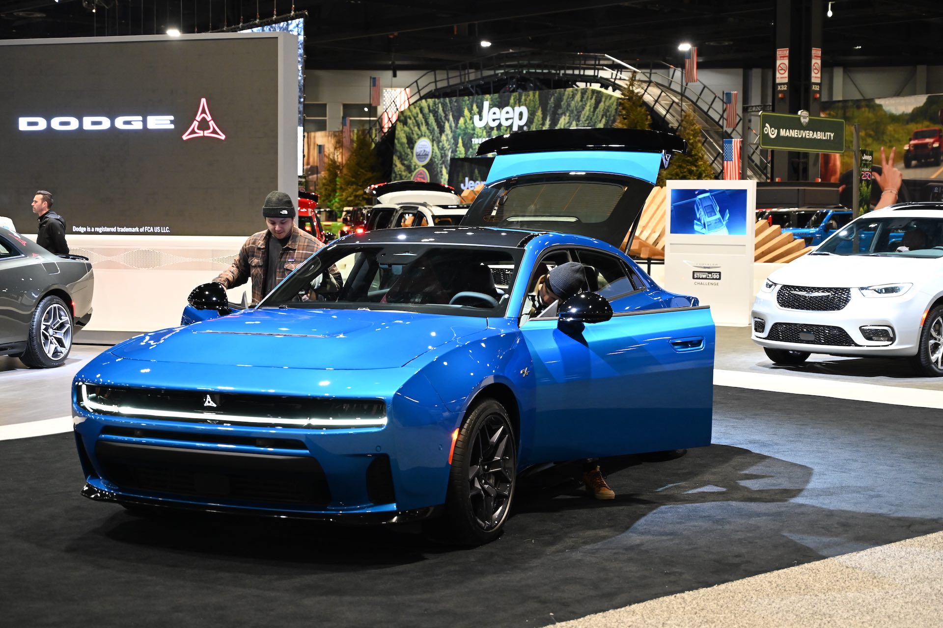 A shot of a blue Dodge Charger on the floor of an auto show, with its doors and trunk open and attendees checking out the interior.