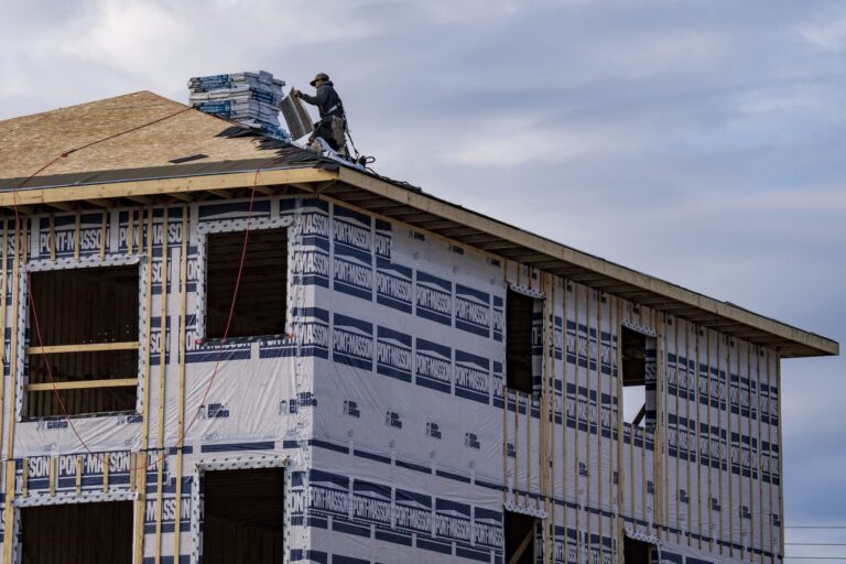 An image of a home under construction. A construction worker is seen on the roof of the house.