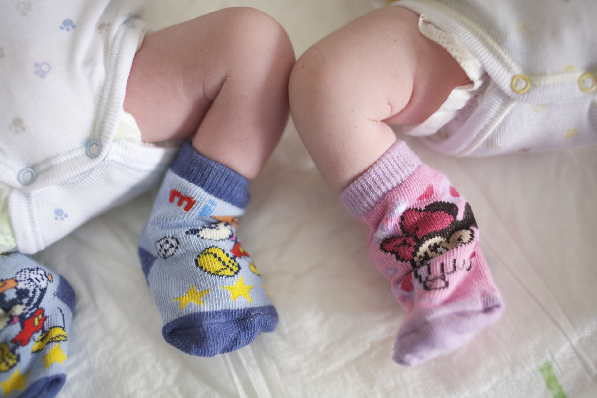 Two babies' feet in colorful socks; one pair in blue with cartoon motifs, the other in pink with a character design.