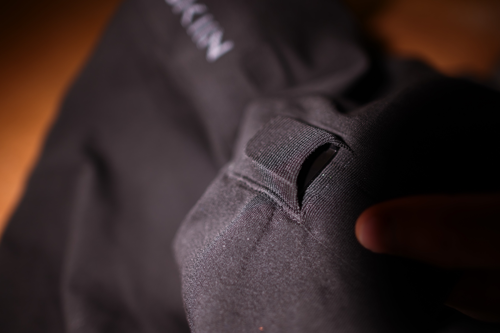 A close-up of a tiny sensor pouch sewn into a black garment. The device in the pouch is close to the size of a human finger that is partially visible in the photo.