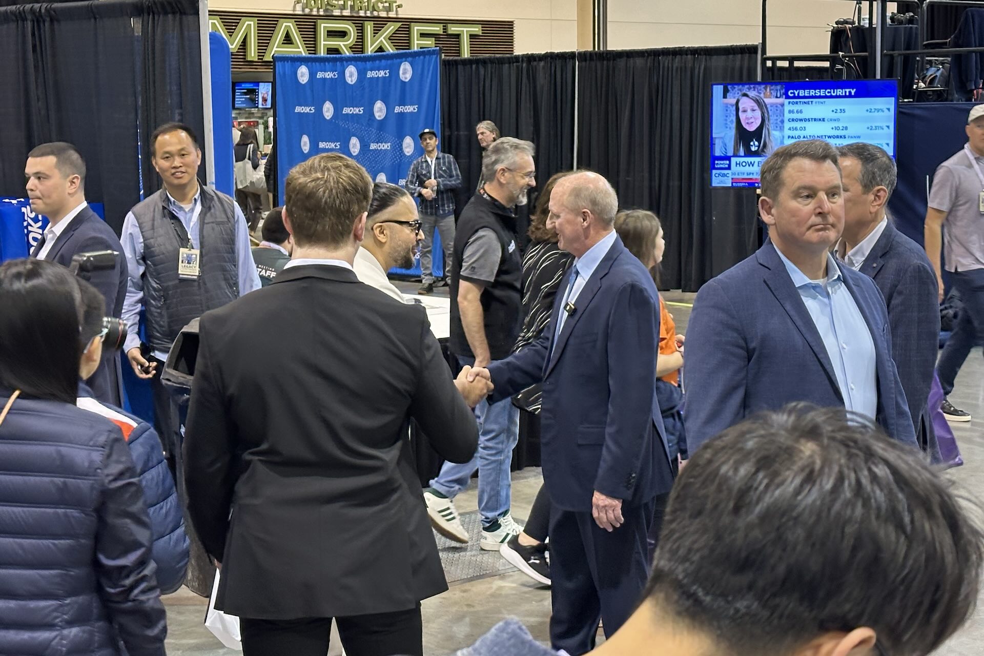 Two men shake hands in the middle of a busy exposition floor.