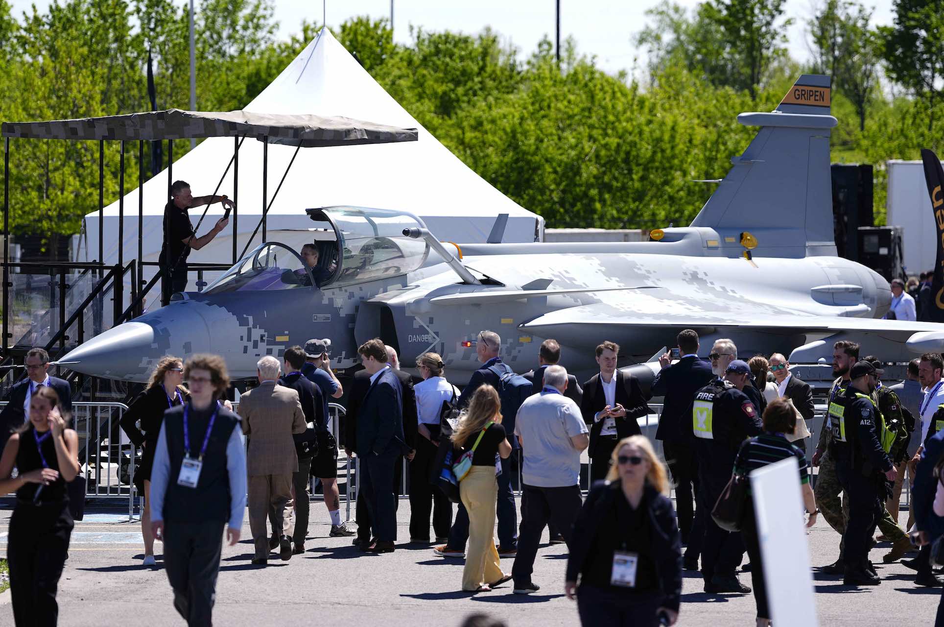 A wide shot of a lineup beside a fighter jet with the word "Gripen" printed on its tail.
