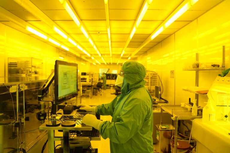 A person wearing a surgical gown, mask and gloves stands facing a screen in a lab.