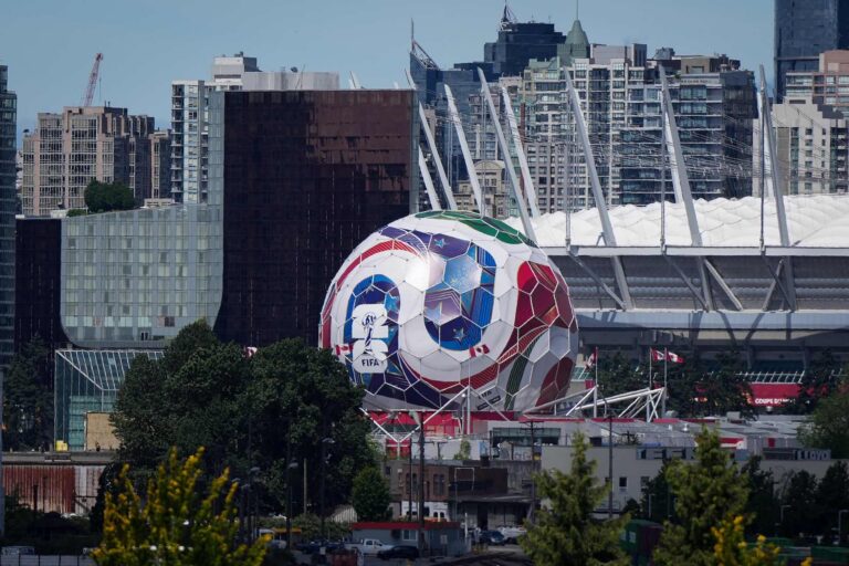 A wide shot of the Vancouver skyline shot from the east, featuring the Science World geodesic dome painted as a FIFA 2026 World Cup soccer ball. B.C. Place stadium appears on the right side of the frame.