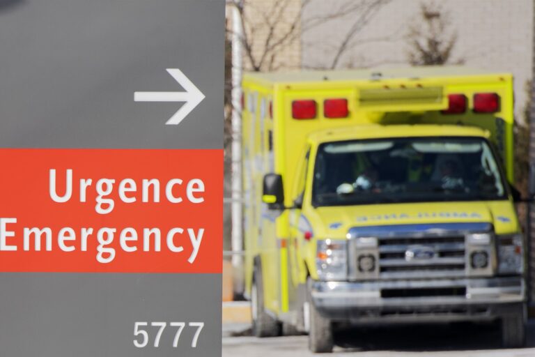 A yellow ambulance is pictured outside of a hospital in Montreal. A red sign in the foreground reads, “Urgence / Emergency.”