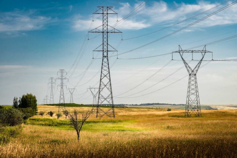 A wide landscape shot of high-tension power lines over green and golden fields in rolling countryside.