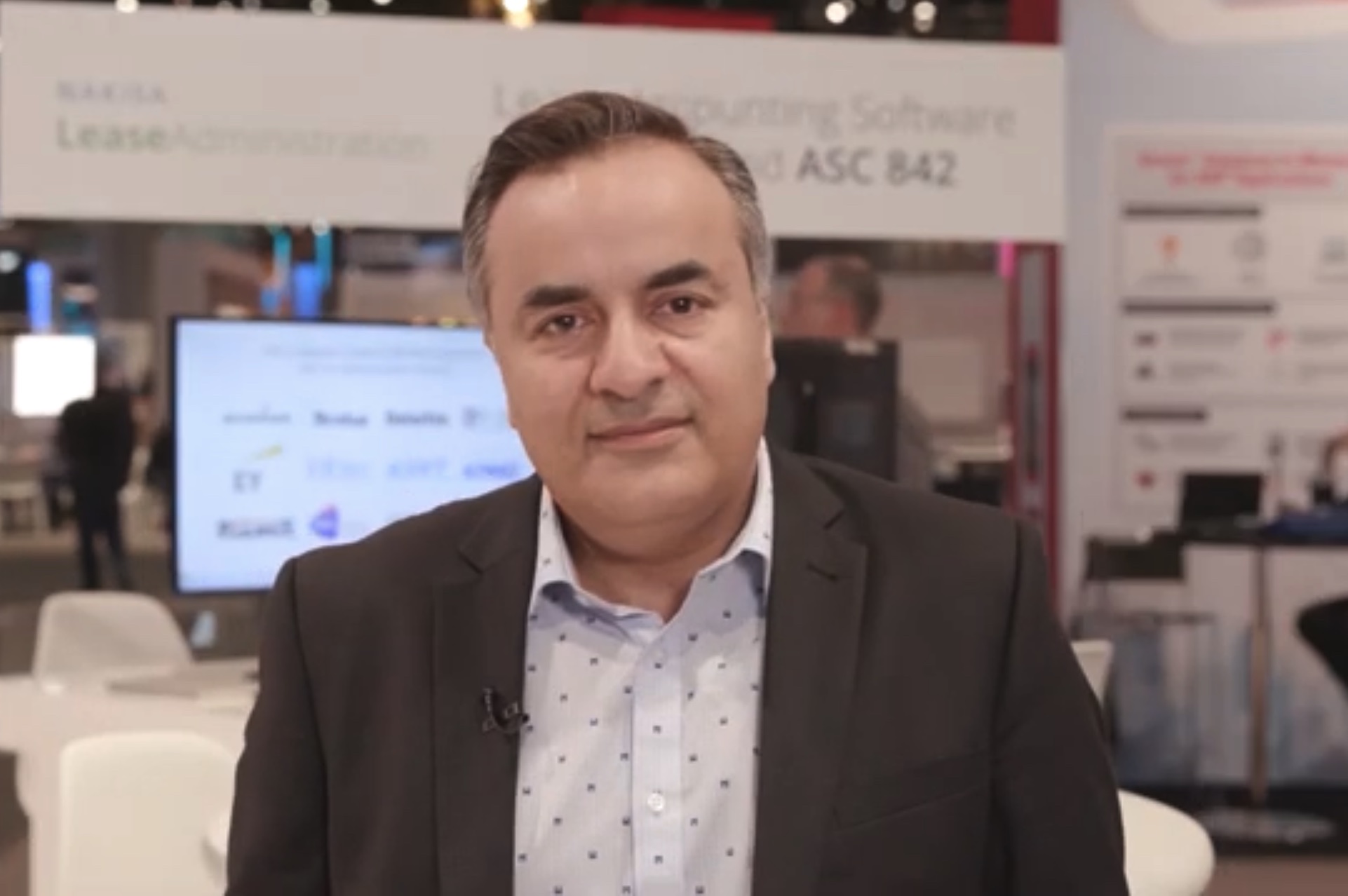 Nakisa CEO Babak Varjavandi in a screencapture from the floor of a tech show. He's wearing a suit jacket and open-collared shirt.
