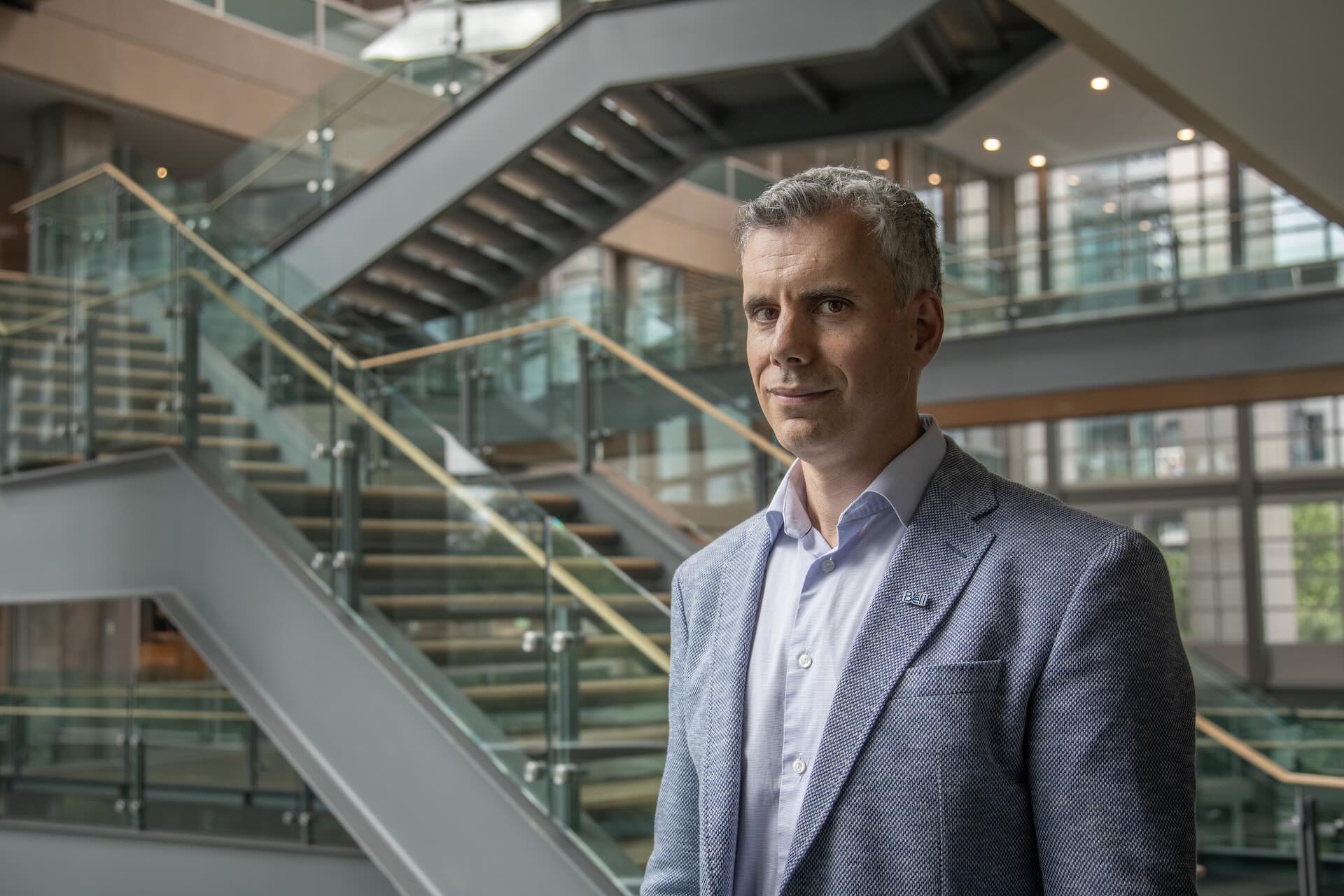 Bell AI Fabric president Michel Richer, stands in a modern office atrium with glass railings, a staircase, and large windows in the background.