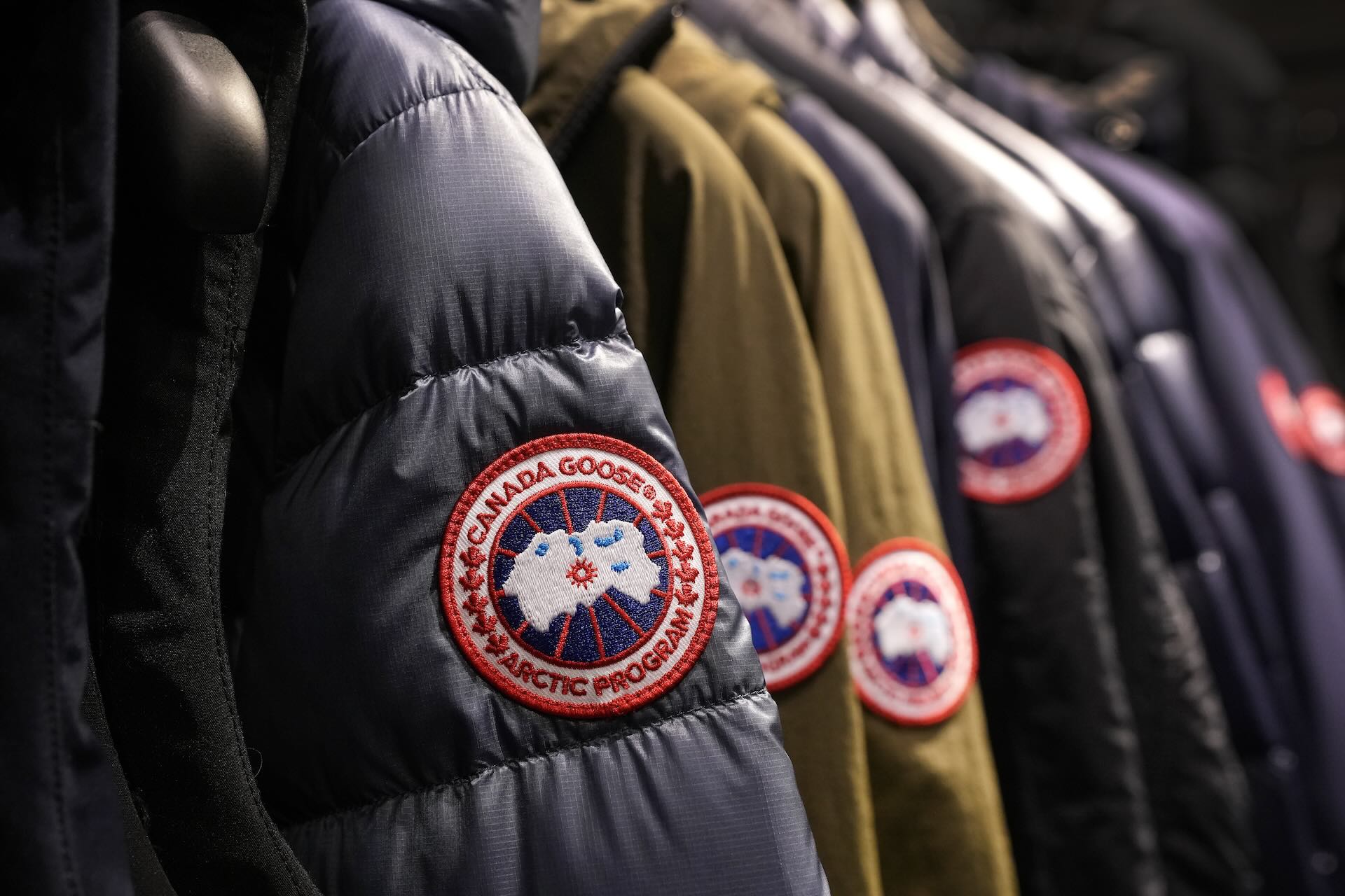 A rack of winter jackets with the Canada Goose arm patch logo visible on each one