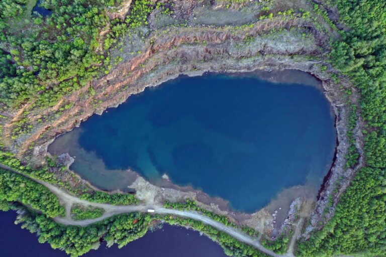 An aerial photo of Kearny mine, a mine surrounded by dense forest, with terraced rock walls that surround a deep blue body of water.