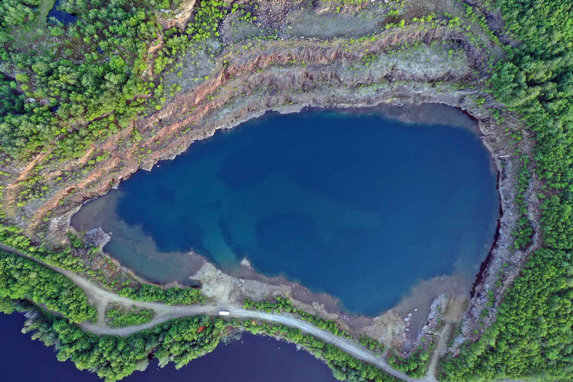 An aerial photo of Kearny mine, a mine surrounded by dense forest, with terraced rock walls that surround a deep blue body of water.