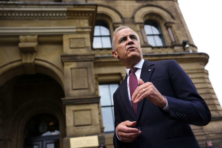 A low-angle shot of Mark Carney taken outside the Prime Minister’s Office. The stone edifice housing the PMO looms in the background.