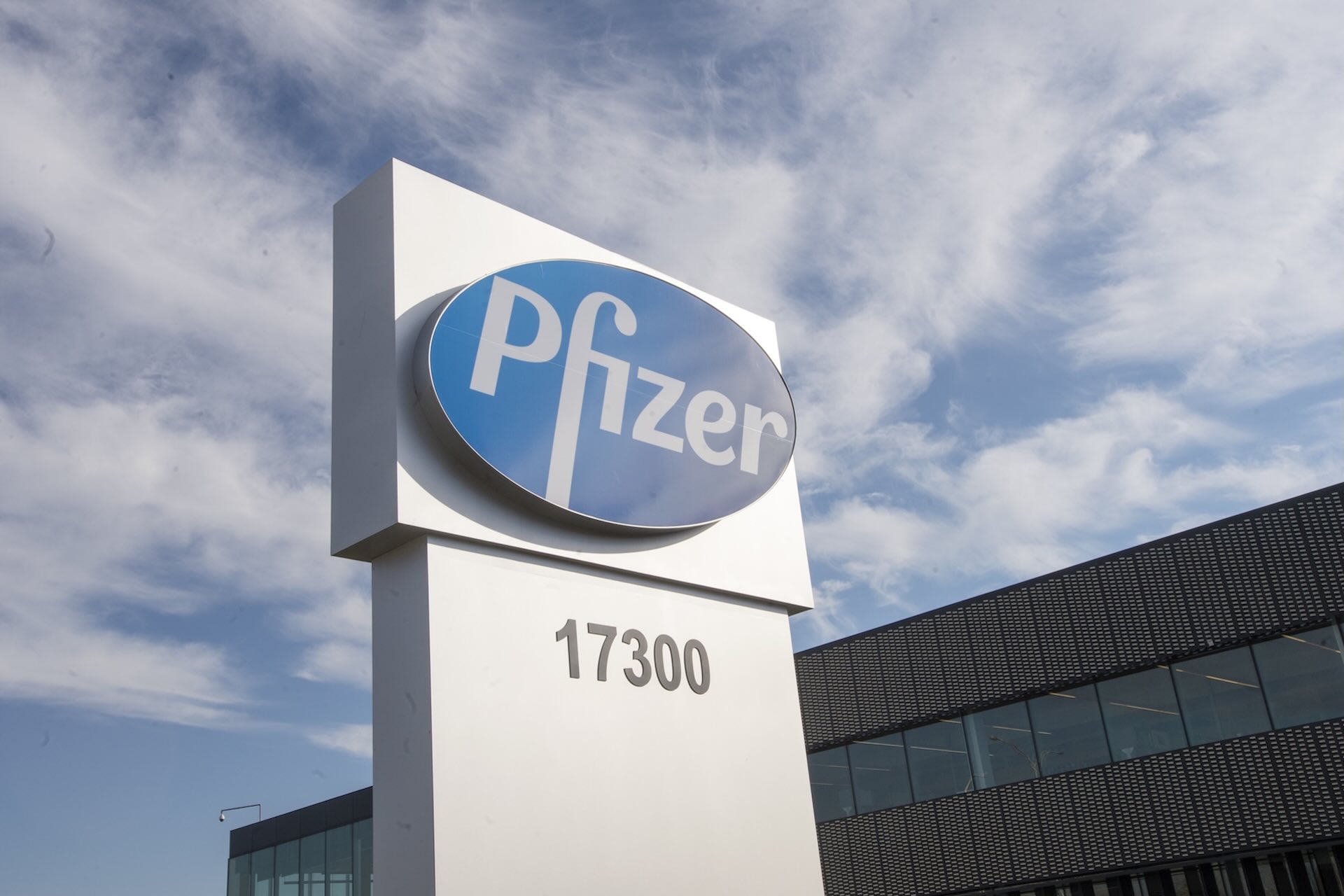 A shot of a sign bearing the Pfizer logo, with a lowrise office building in the background.