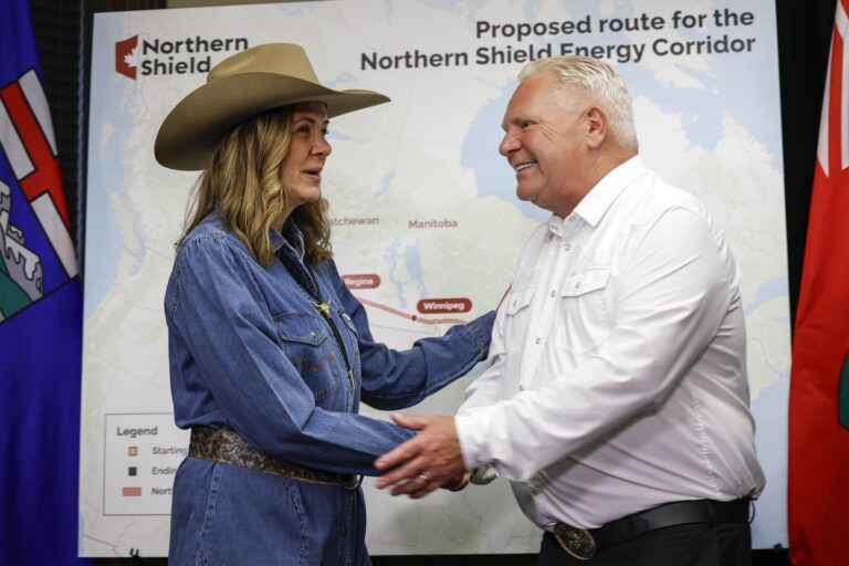 Danielle Smith and Doug Ford shake hands in front of a map with a Northern Shield logo and a heading saying “Proposed route for the Northern Shield Energy Corridor.”