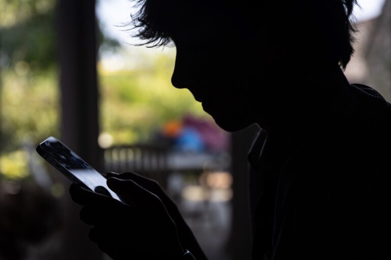 A silhouette shot of a teenaged boy looking at his phone.
