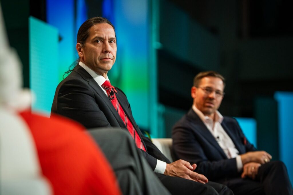 Bill Lomax, president and CEO of First Nations Bank of Canada, listens during a panel on stage. Canada Infrastructure Bank CEO Ehren Cory is seated next to him. 