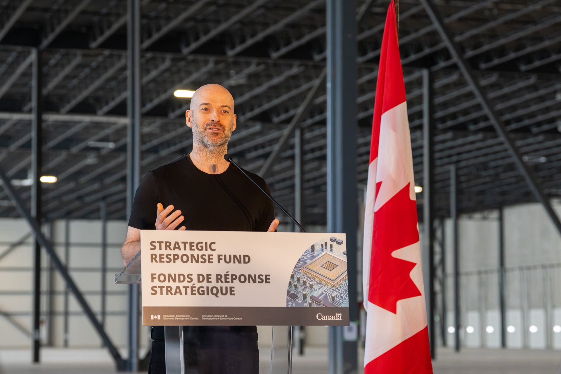 Christian Weedbrook stands in a vacant warehouse next to a Canadian flag at a podium labelled for the Strategic Response Fund.