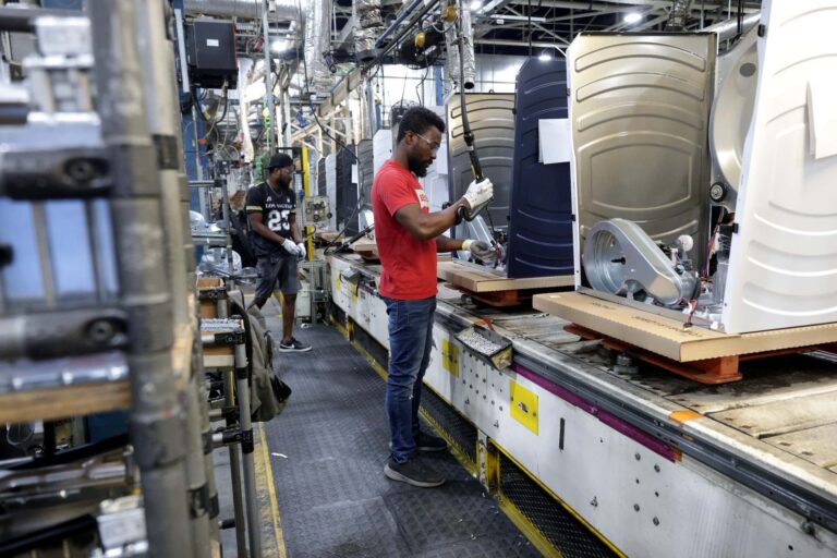 A shot of two factory workers building dryers on an assembly line.