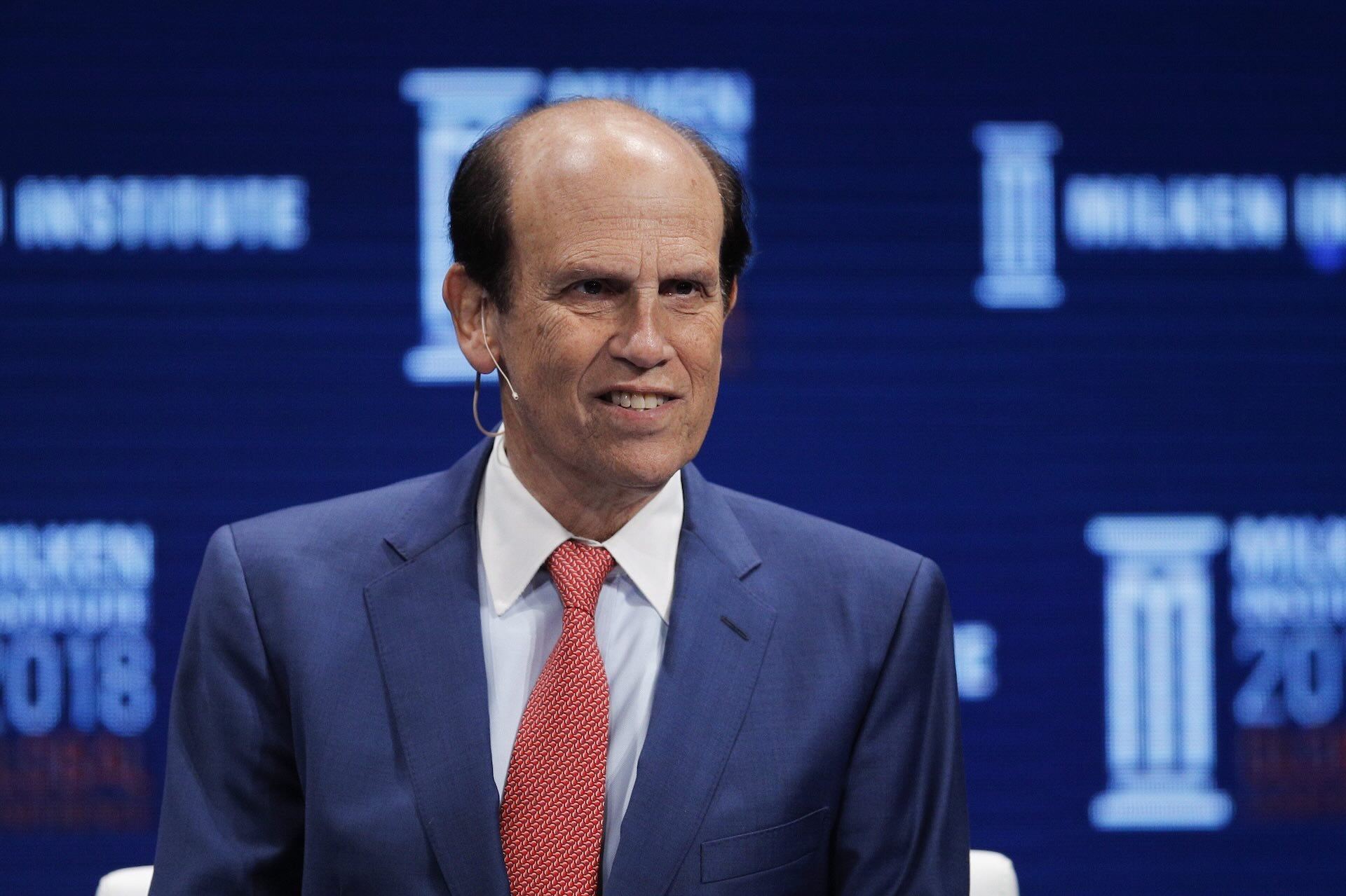 Financier Michael Milken leads a discussion at the Milken Institute Global Conference in Beverly Hills, Calif. He wears a blue suit and a red tie against a blue background.