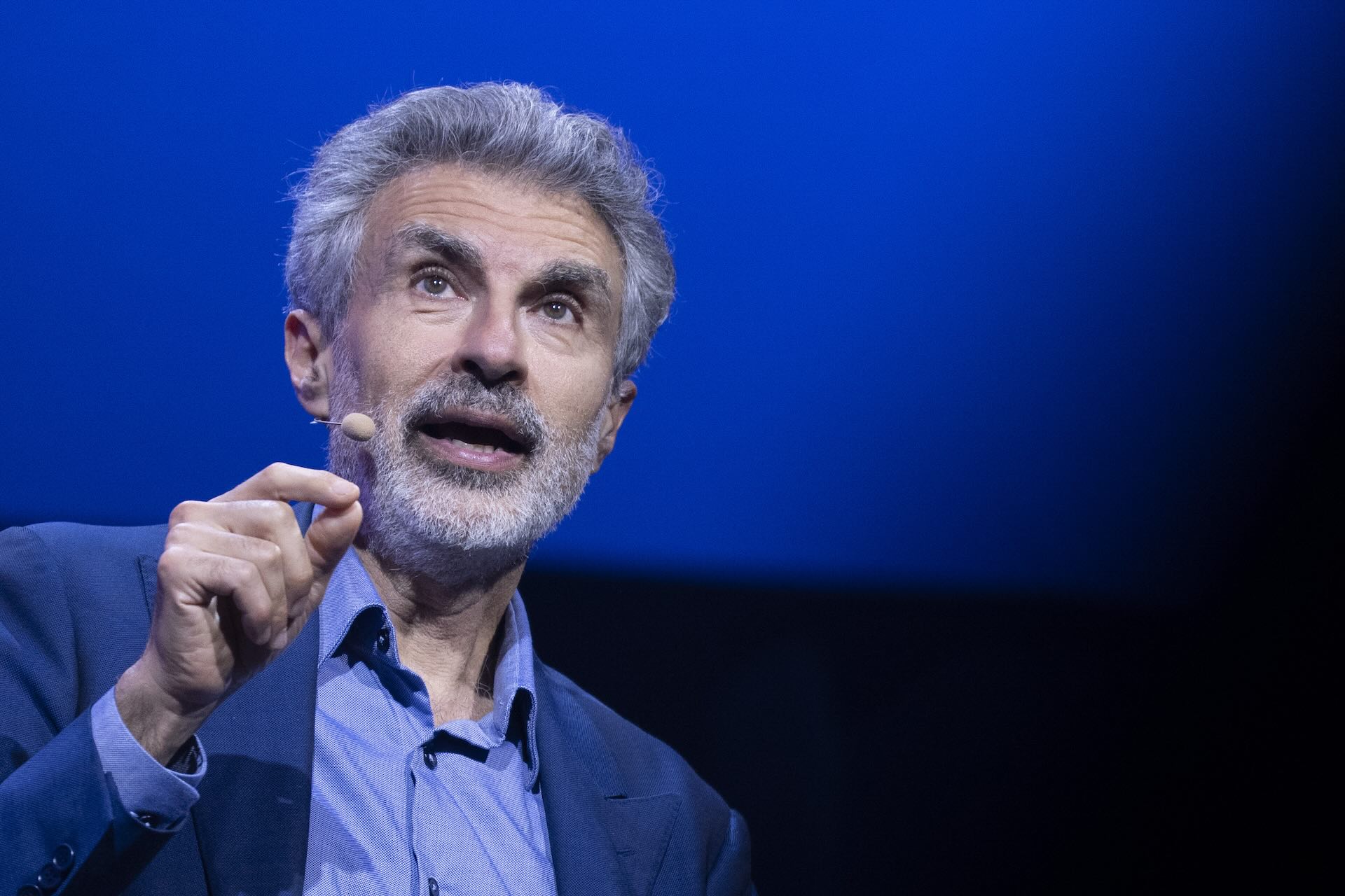 Close-up of Yoshua Bengio speaking on stage with an out-of-focus blue and black background