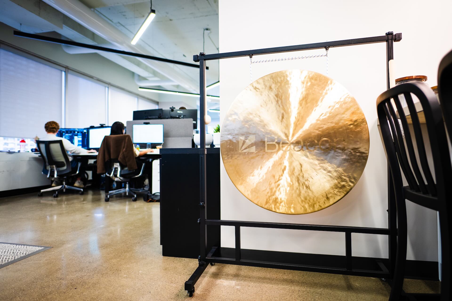 A gold gong with with the phrase "Beacon" etched into it, hanging off a black metal rolling frame in an office