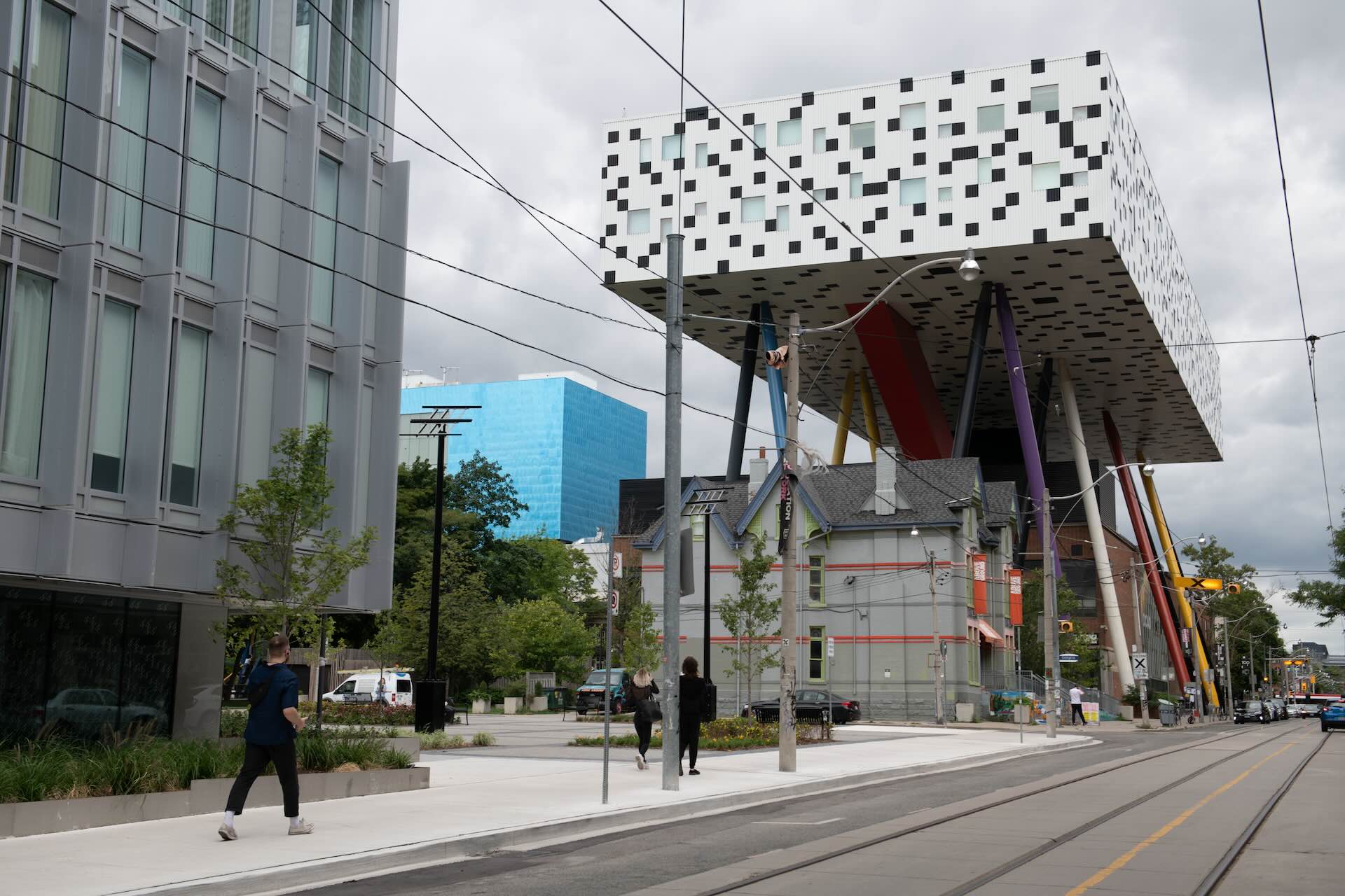 An exterior view of The Ontario College of Art and Design, a modern white block with checkerboard squares on the side, held above an older building by a series of brightly coloured poles.