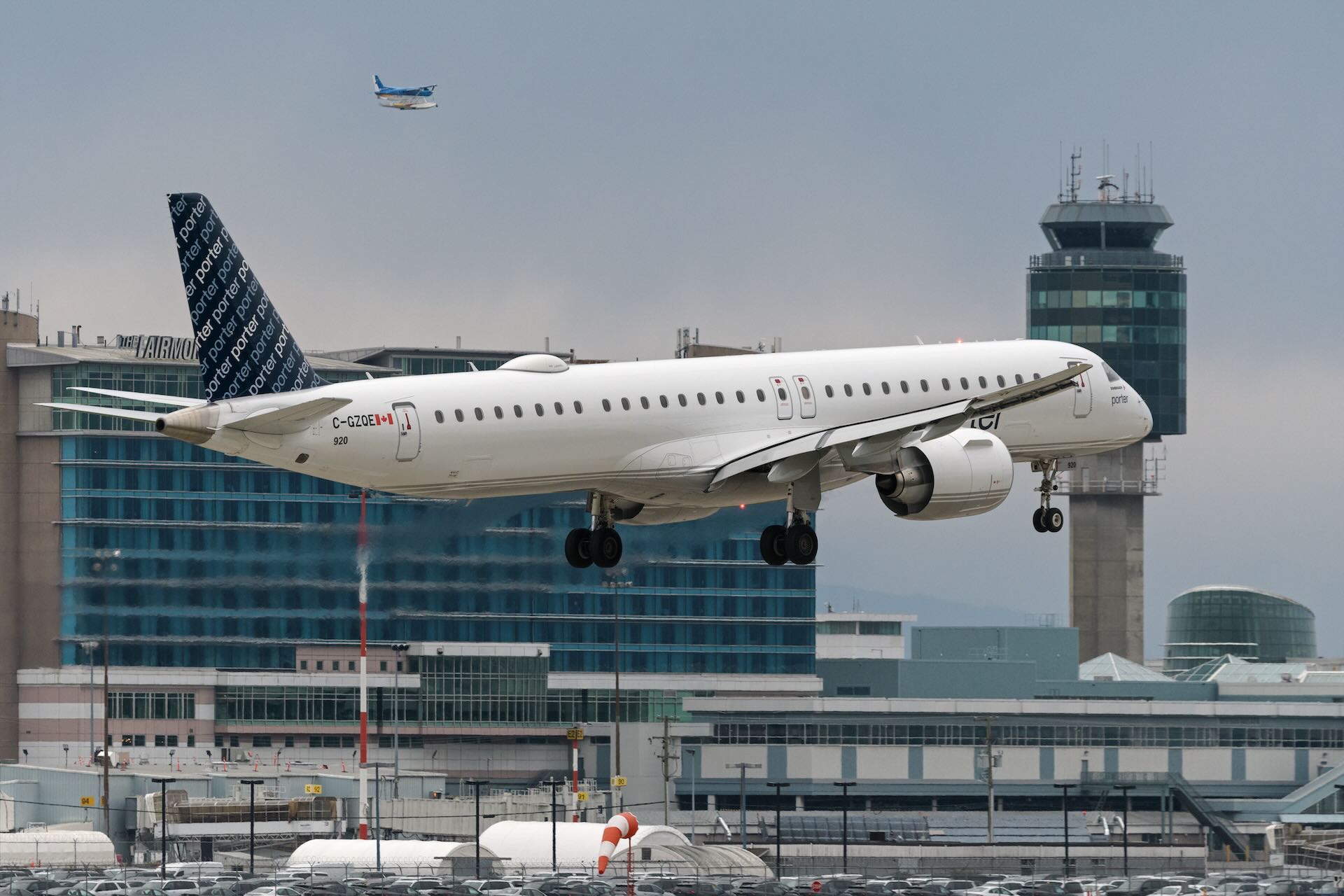 A Porter Airlines plane lands at Vancouver's YVR airport, with buildings and a traffic control tower visible in the background